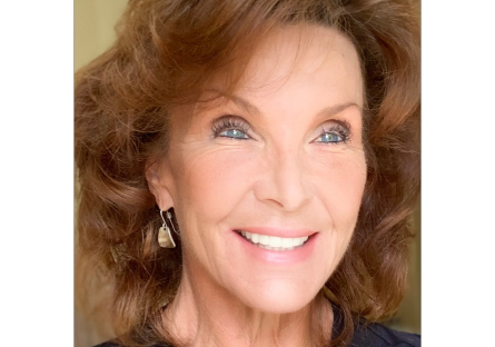 A close-up of a smiling woman with wavy light brown hair and earrings.